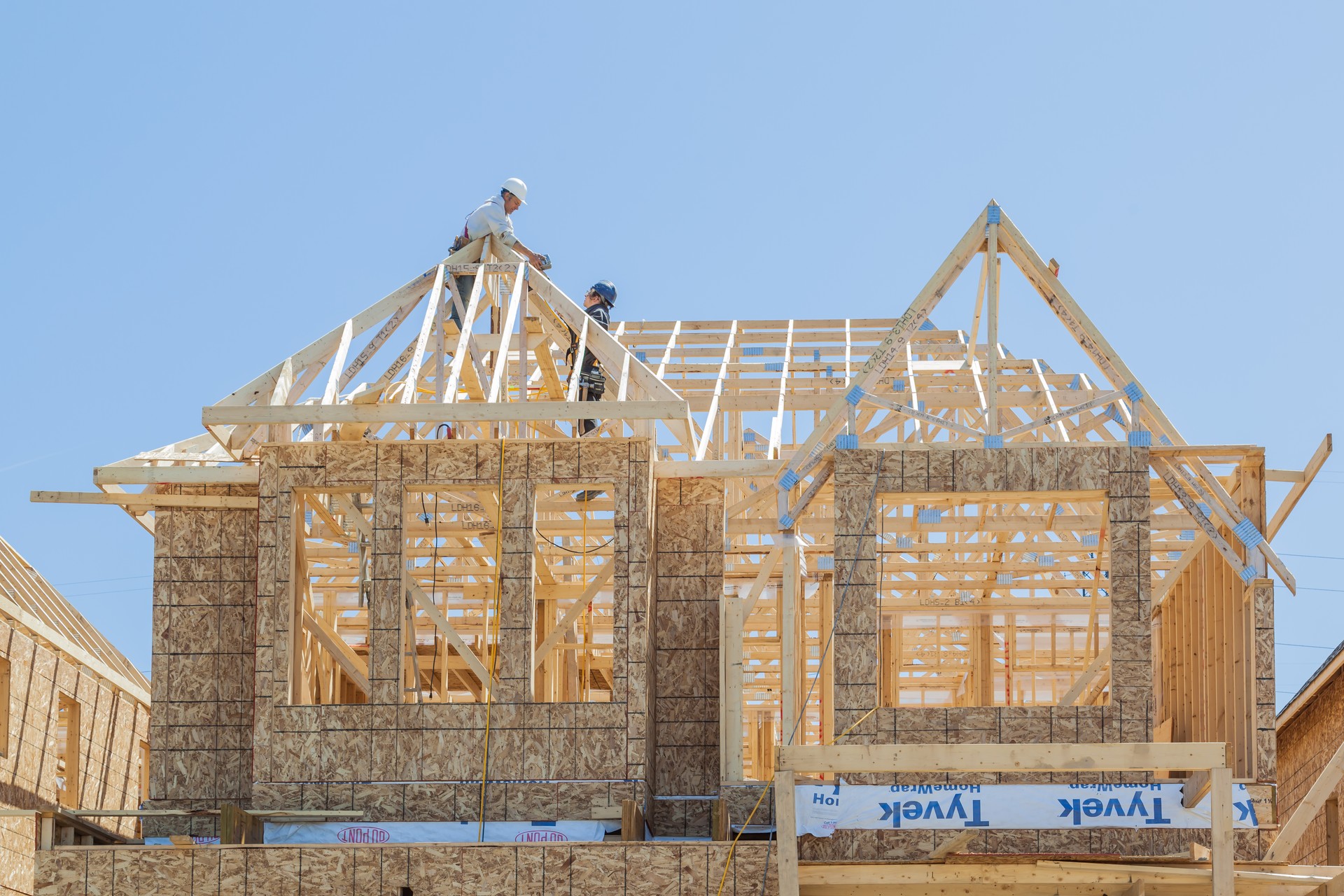 New house under construction, two workers installing roof truss.